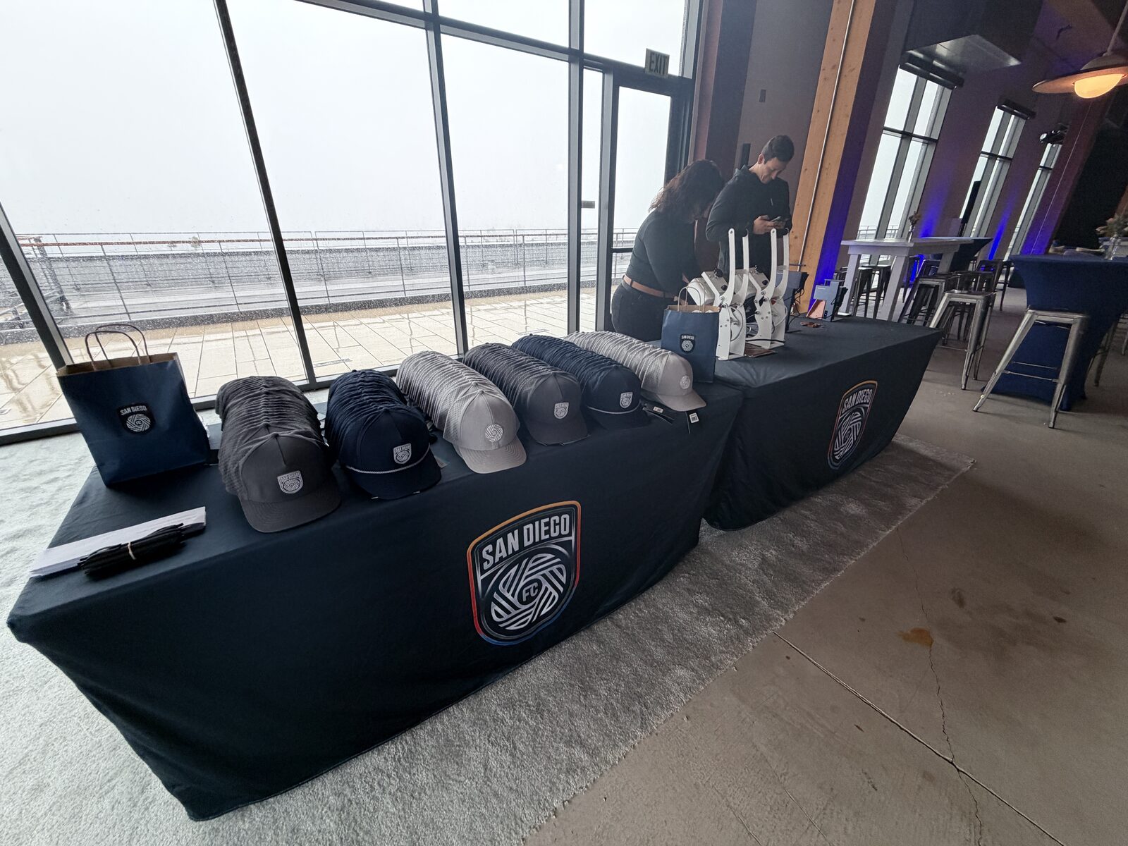 Embroidered caps lined up in rows on black merch tables at a waterfront venue