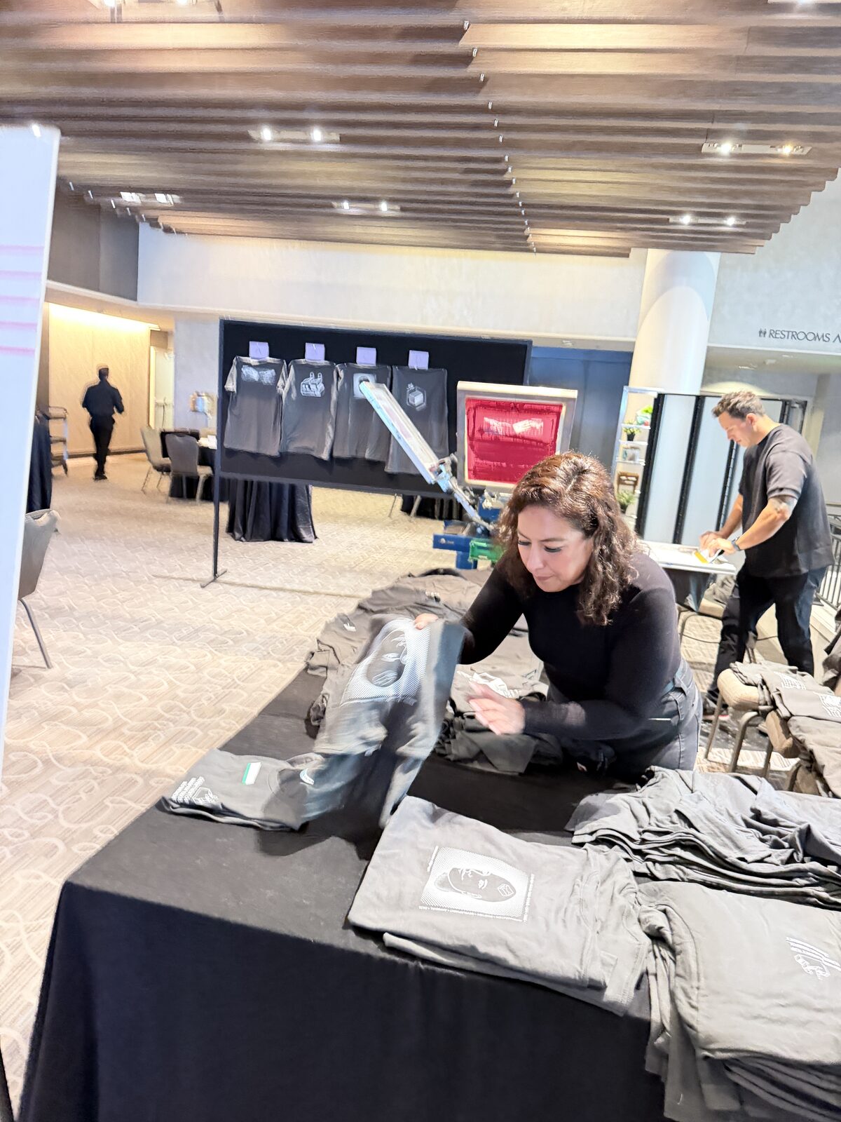 Crew member folding freshly printed favor shirts at a draped reception merch table