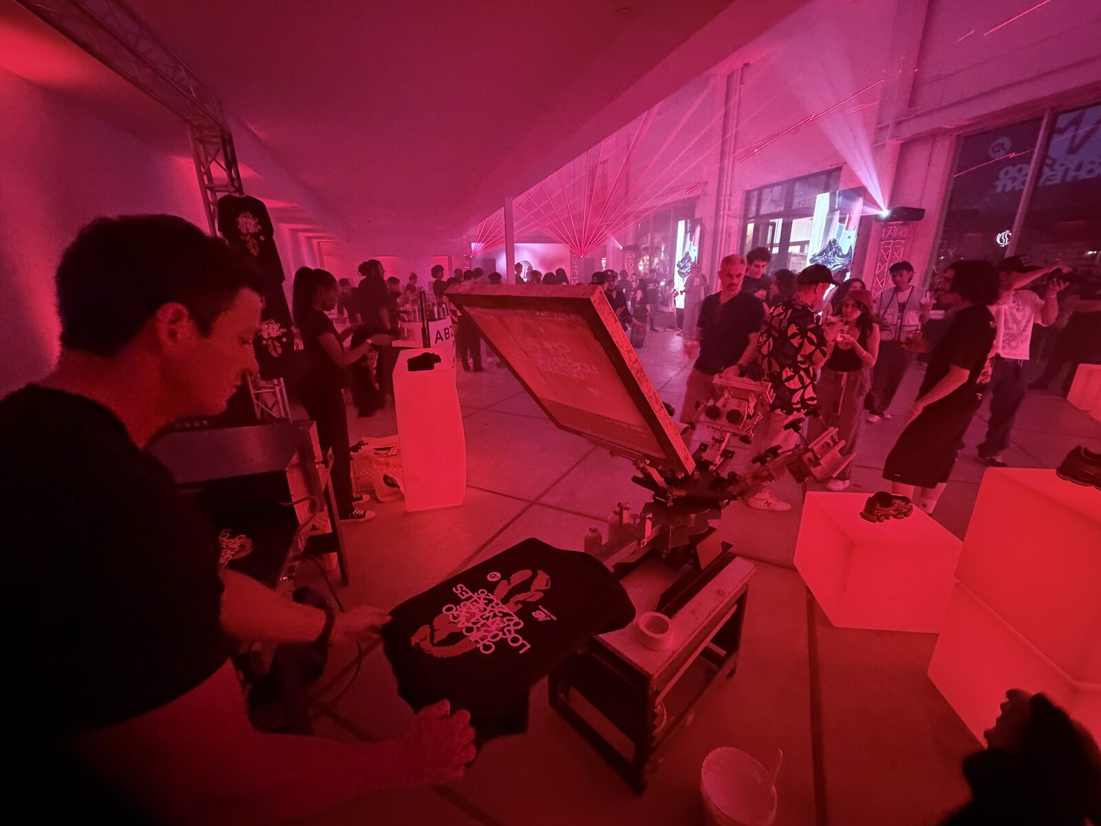 Printer lifting a freshly printed black shirt off the press at a red-lit night event